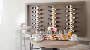 Ein Frühstücksarrangement mit einer Auswahl an Gebäck und Saft, ein Weinregal im Hintergrund und ein Blumenstrauß auf einem Tisch.