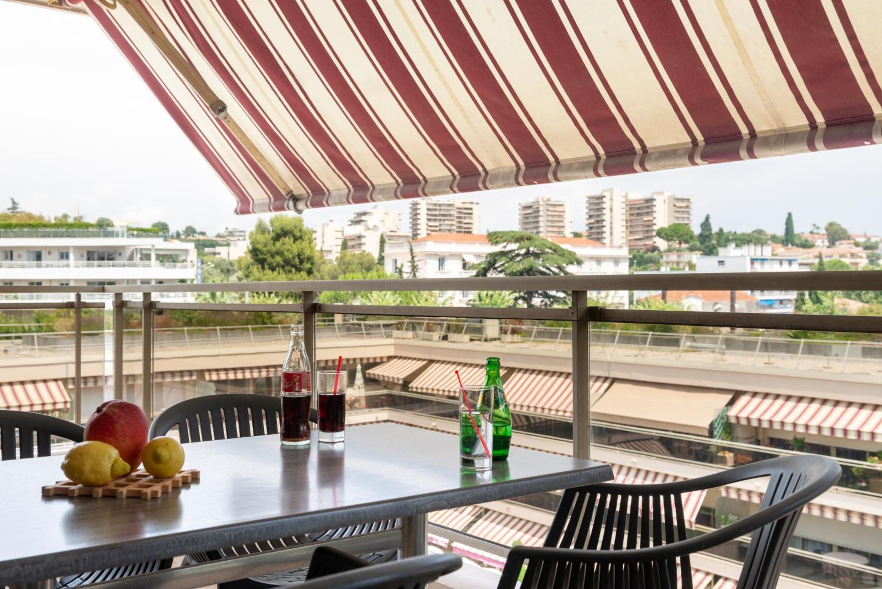 Un balcon avec une table dressée pour deux personnes, agrémentée d’une bouteille de soda, d’un verre et d’une assiette de fruits.