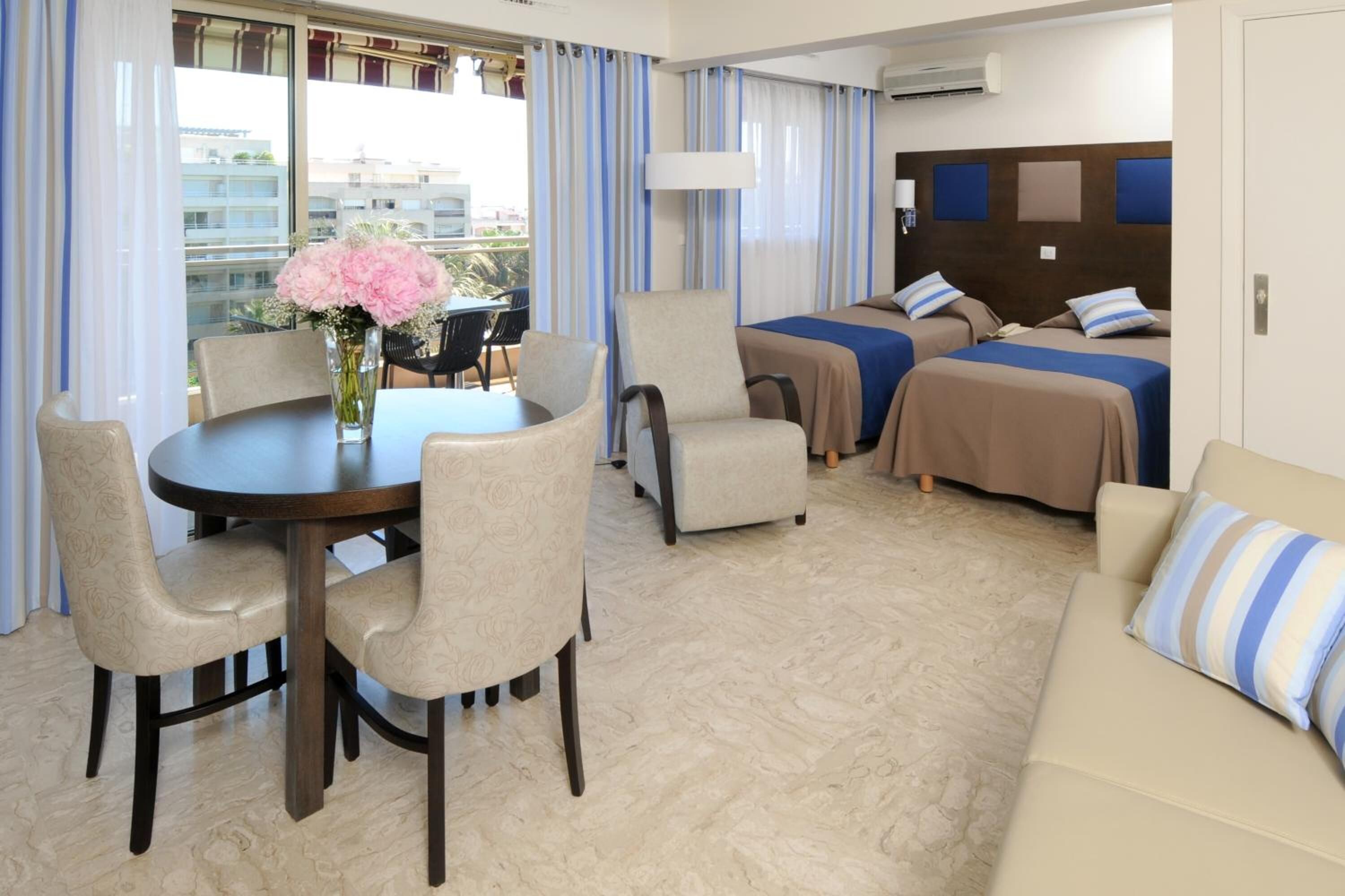 A hotel room with a dining table, two armchairs, a sofa, and a bed with two pillows.