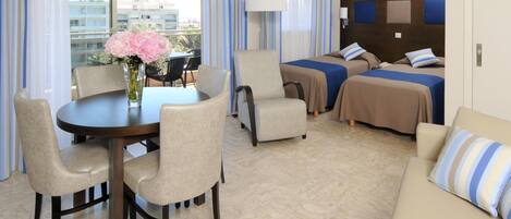 A hotel room with a dining table, two armchairs, a sofa, and a bed with two pillows.