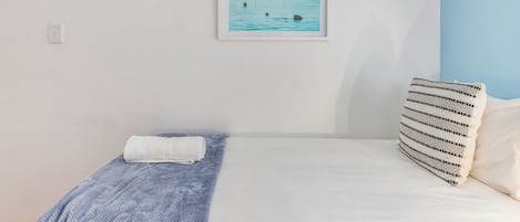 A bedroom with a bed, a pillow, a framed picture of a pier, and a wall socket.