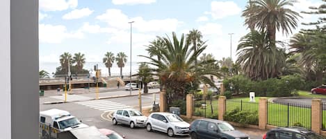 A parking lot with several cars, a pedestrian crossing, and palm trees in the background.