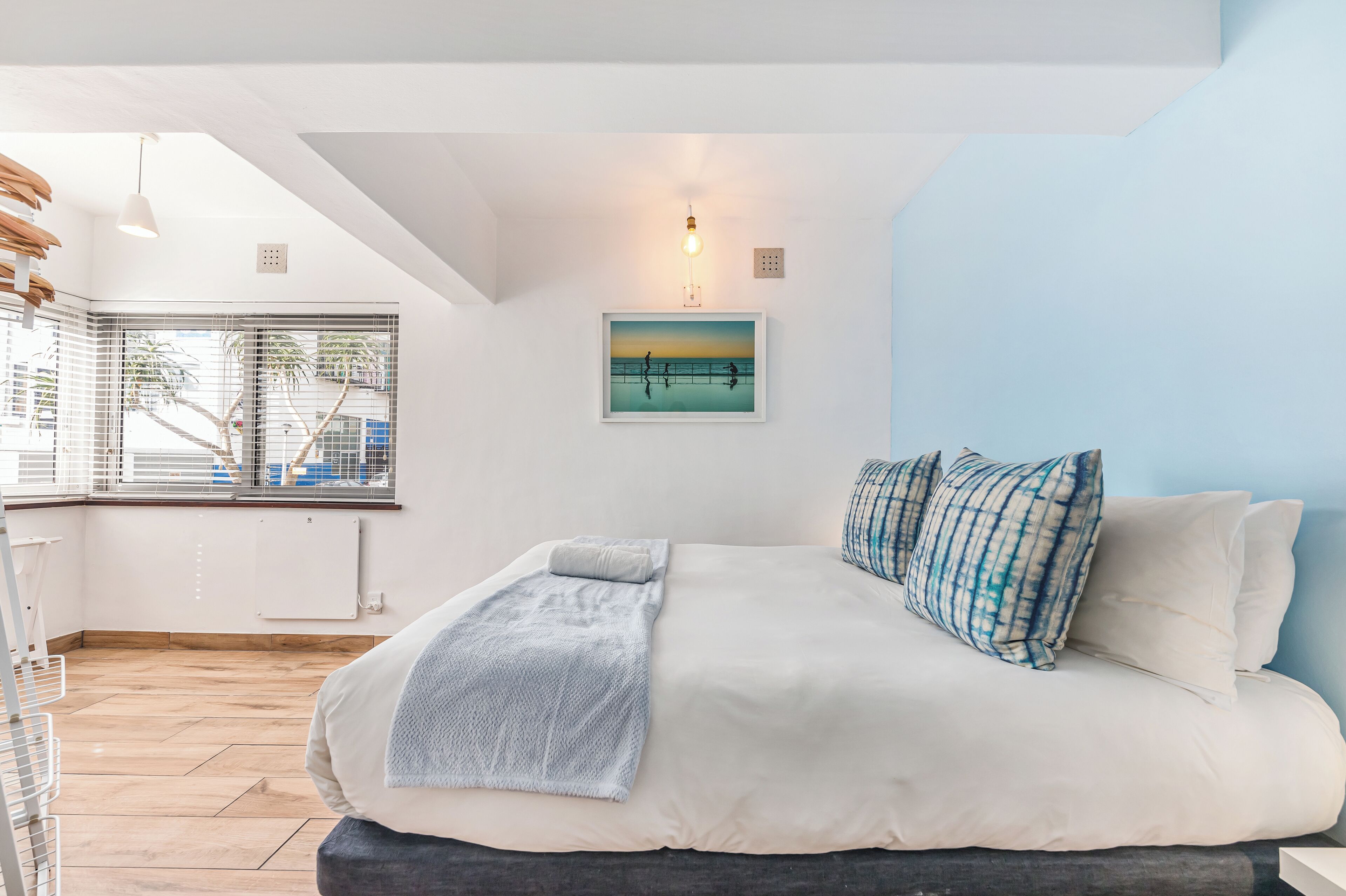 Un dormitorio moderno con una cama grande, una ventana con persianas, una lámpara de pared y un cuadro enmarcado.