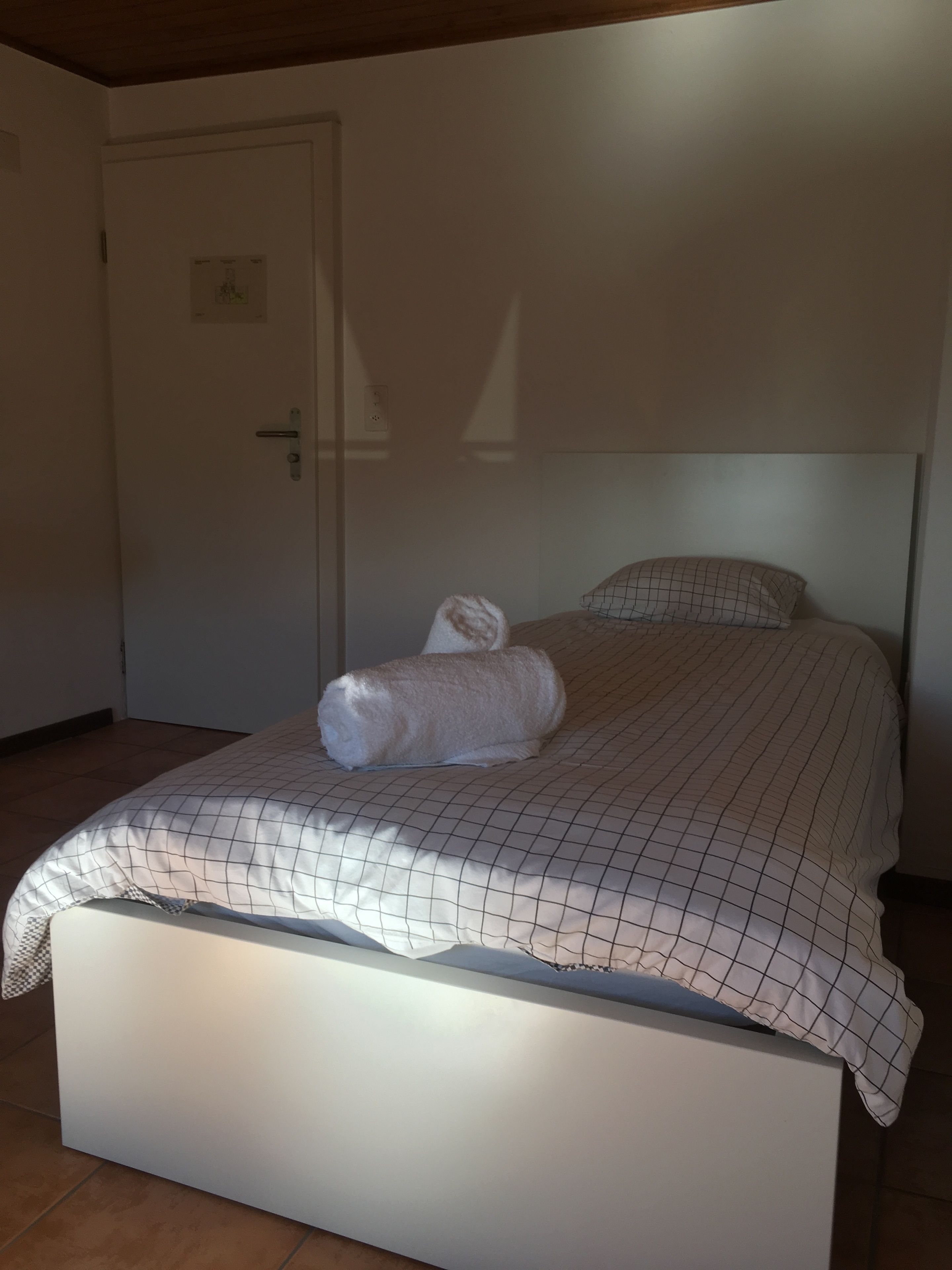 A bedroom with a bed, a white door, and a tiled floor.