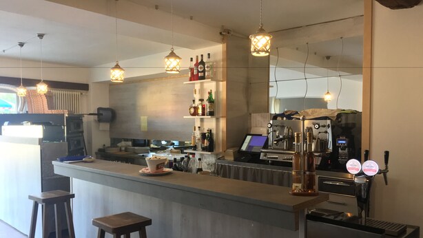 A modern kitchen with a bar area, bar stools, a coffee machine, and various bottles on shelves. - Albergo Ristorante Belcantone (Novaggio)