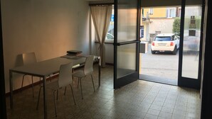 A room with a dining table, chairs, a sliding glass door leading outside, and a view of a parked car. - Albergo Ristorante Belcantone (Novaggio)