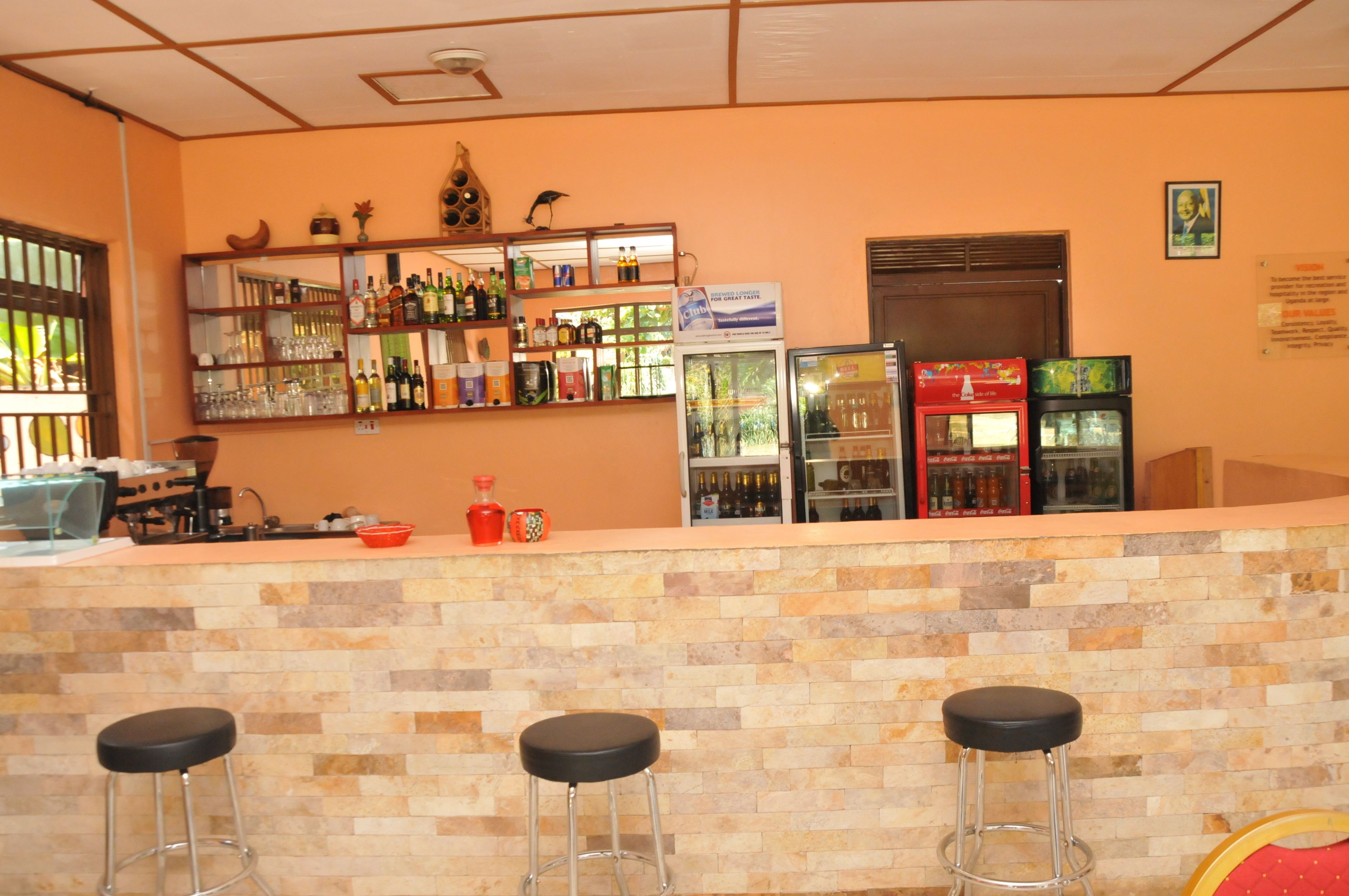 A bar area with a tiled counter, stools, shelves with bottles, and a refrigerator.