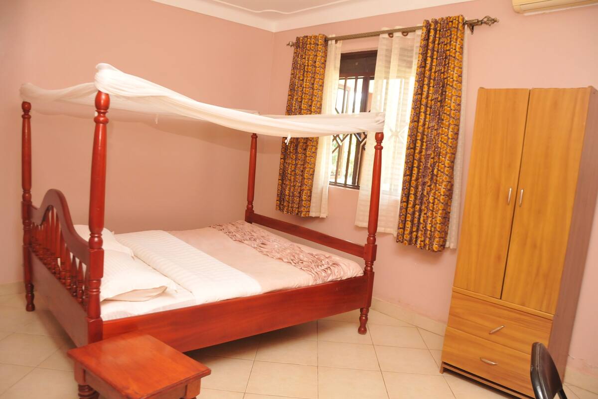A bedroom with a four-poster bed, a wooden wardrobe, and curtains.