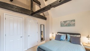 Un dormitorio con una cama grande, puertas blancas, un espejo y un cuadro en la pared.