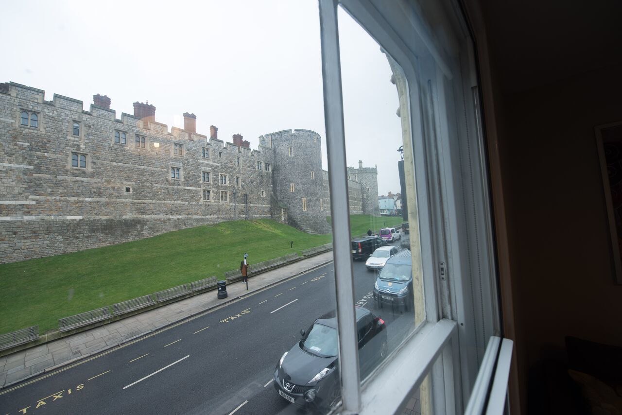Vista de un edificio histórico de piedra con estructura similar a un castillo, una carretera con coches y una zona verde.