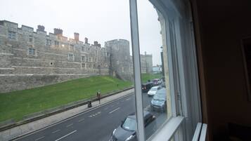 Vista de un edificio histórico de piedra con estructura similar a un castillo, una carretera con coches y una zona verde.