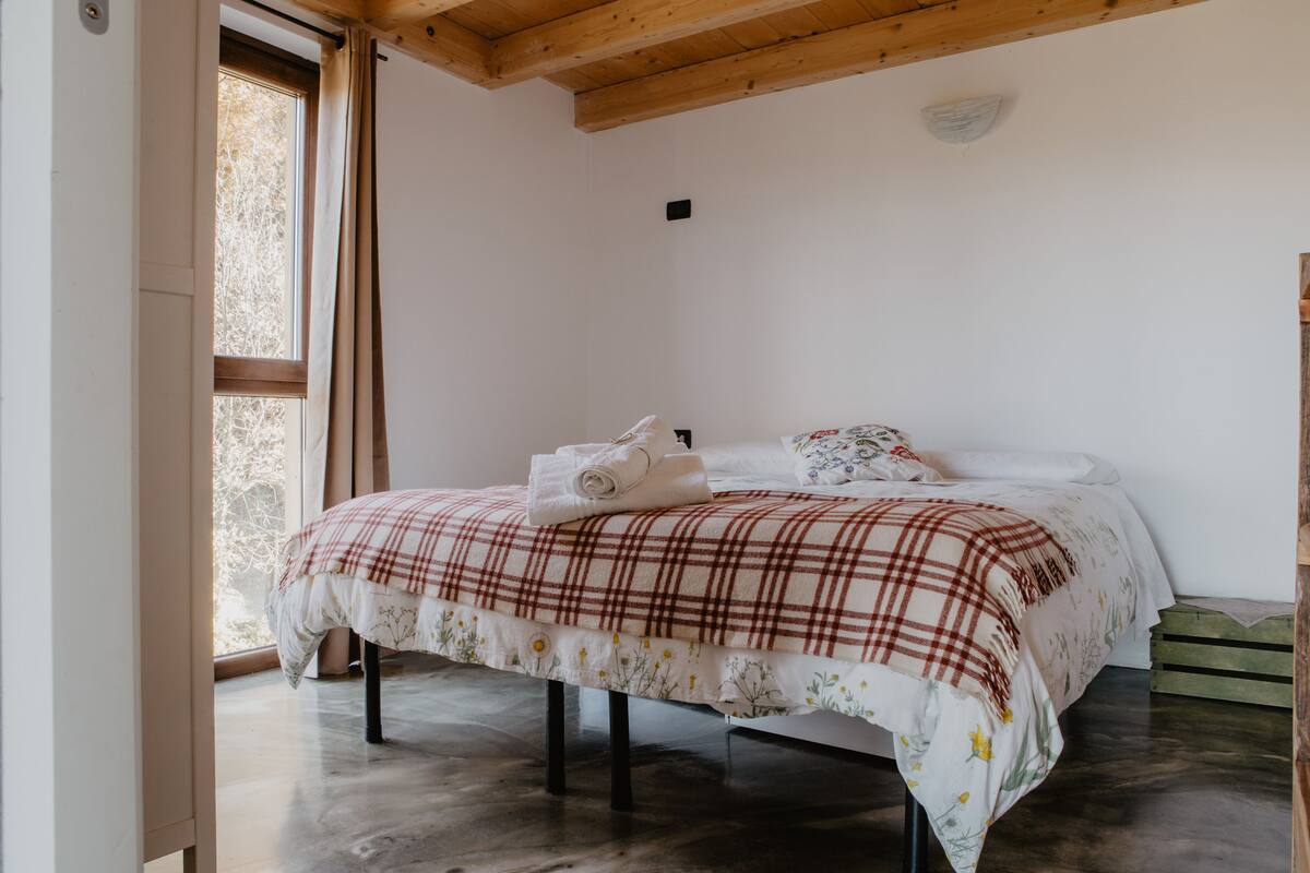 A bedroom with a bed, a window, and a wooden ceiling.