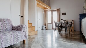 A spacious living area with a sofa, a dining table with chairs, and a staircase leading to an upper level. - Agriturismo Le Piagge (Ponzone)