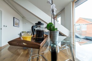 A modern kitchen with a coffee maker, a glass of orange juice, and a potted orchid on a glass table. - Hampden Apartments - The Elizabeth (Windsor)