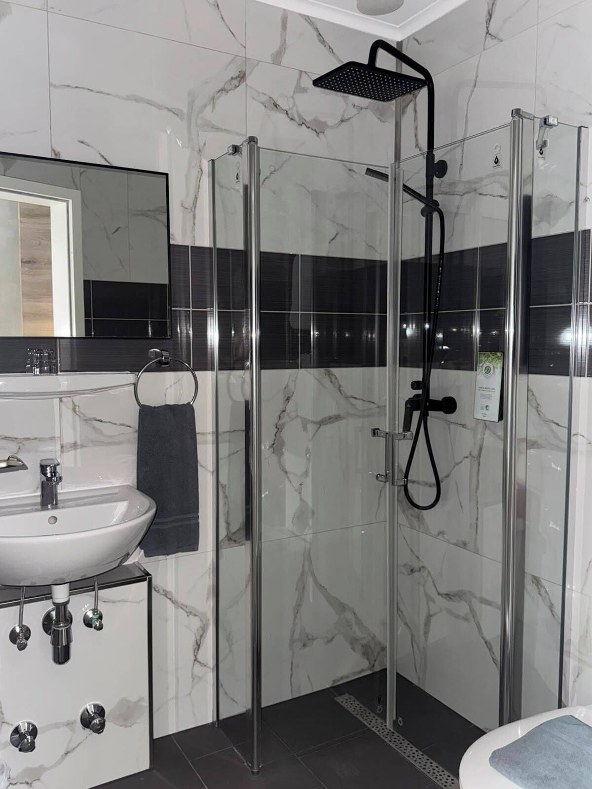 Un baño moderno con ducha envuelta en vidrio, un lavamanos con espejo y un perchero para toallas.