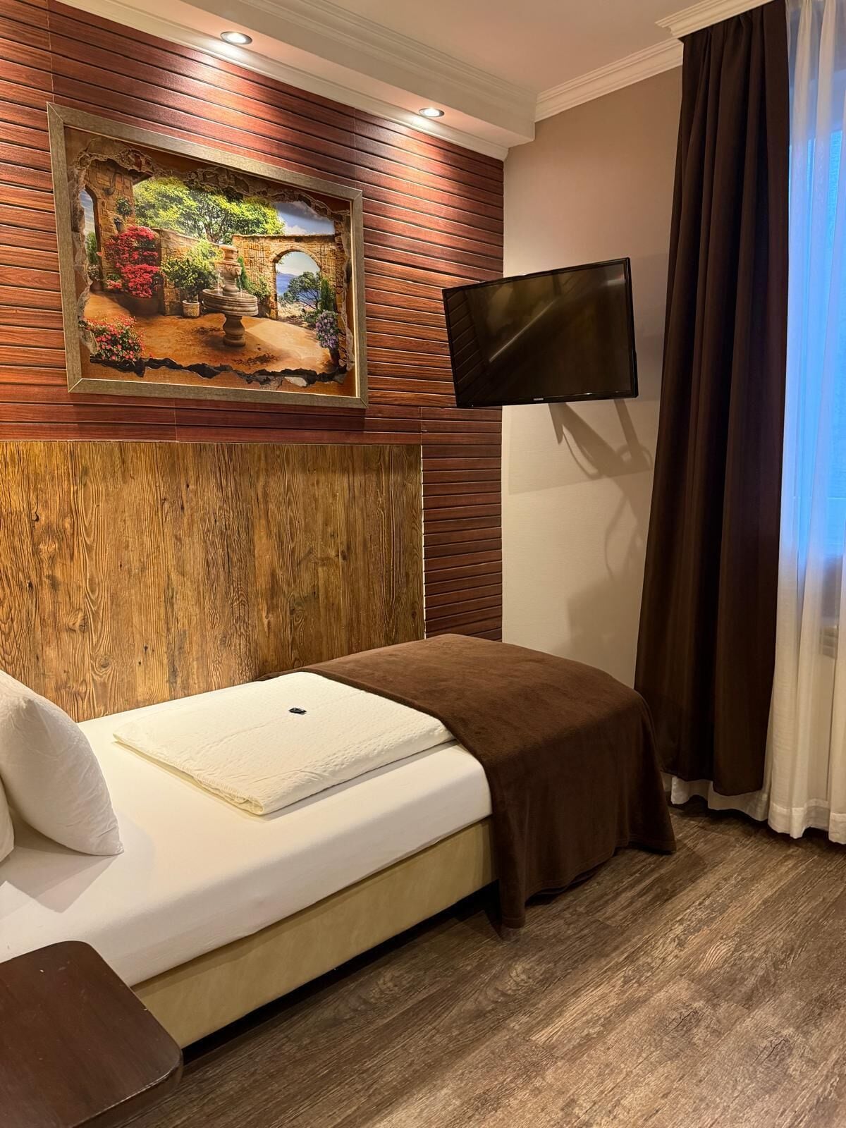 Quarto de hotel com cama, televisão montada na parede e um quadro pendurado.