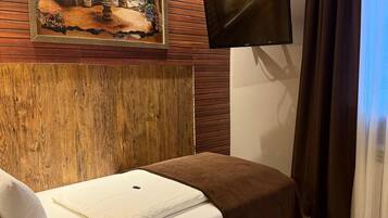 A hotel room with a bed, a mounted television, and a wall-mounted painting.
