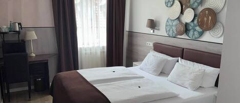 Quarto de hotel com uma cama, uma escrivaninha, um abajur e uma parede com pratos decorativos.