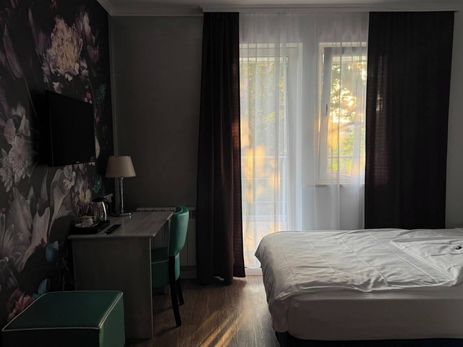A hotel room with a bed, a desk with a lamp, a chair, and a television on the wall.