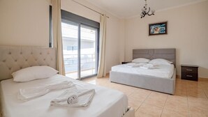A hotel room with two beds, a large window with curtains, a chandelier, and a painting on the wall. - Hotel Primavera (Sarandë)