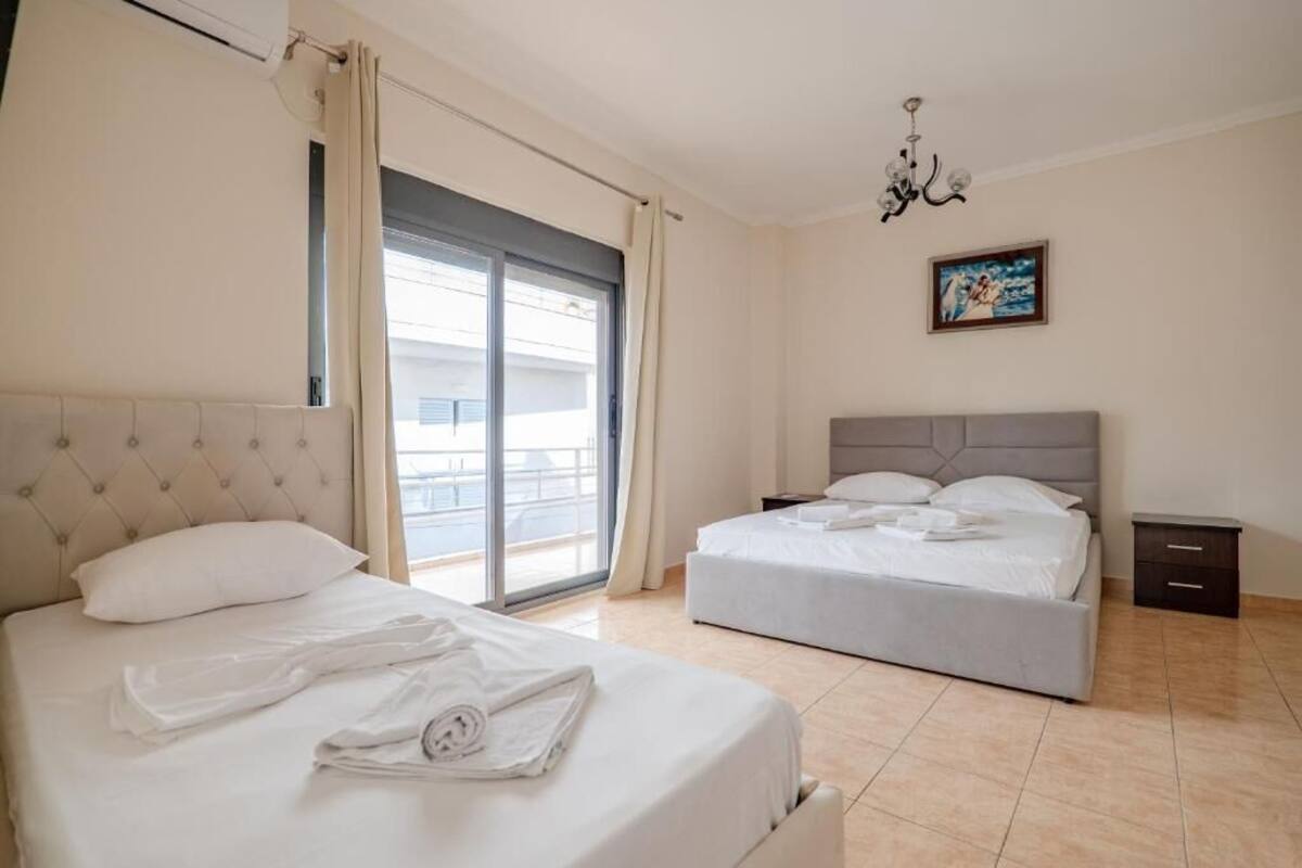 Une chambre d’hôtel avec deux lits, une grande fenêtre avec des rideaux, un lustre et un tableau au mur.