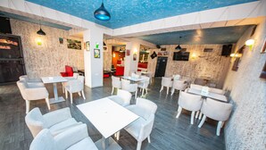 A restaurant with white tables and chairs, a blue ceiling, and a stone wall design. - Hotel Primavera (Sarandë)