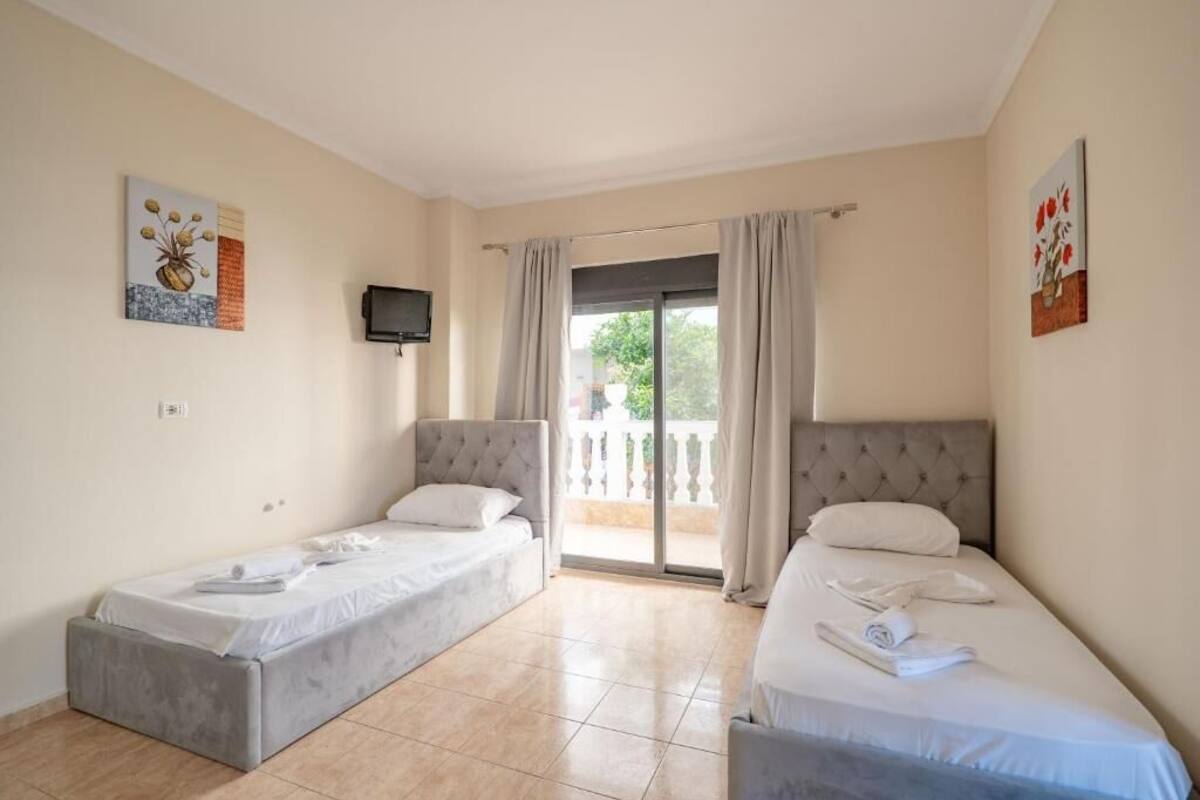 Une chambre d’hôtel avec deux lits simples, une télévision et un balcon avec des rideaux.