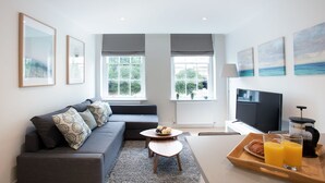 A modern living room with a sofa, coffee table, and breakfast tray with croissants and juice. - Hampden Apartments - The George (Windsor)