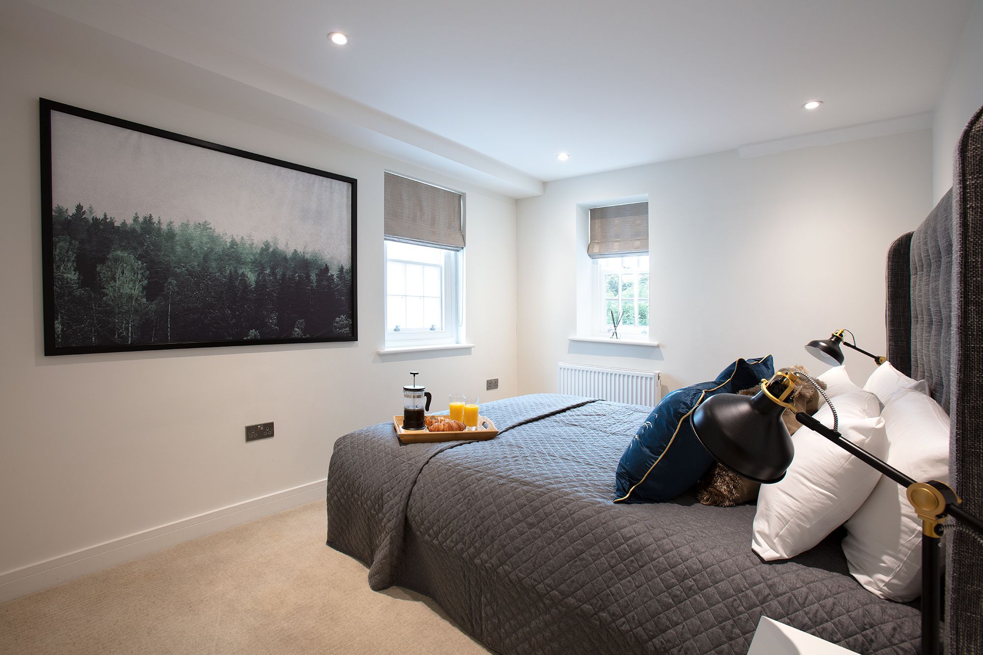 A bedroom with a large bed, a bedside table with a lamp, a window, and a painting on the wall.