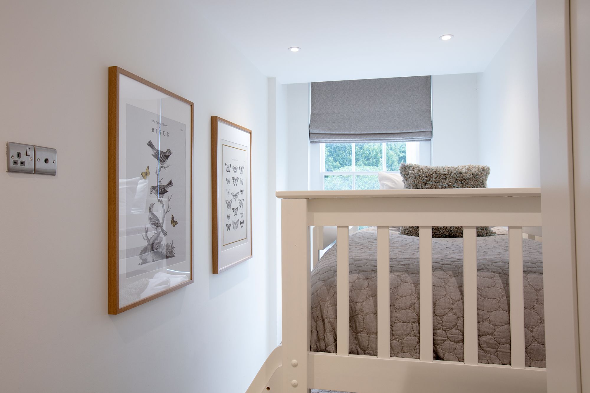 A bedroom with a crib, a window with a view, and two framed pictures on the wall.