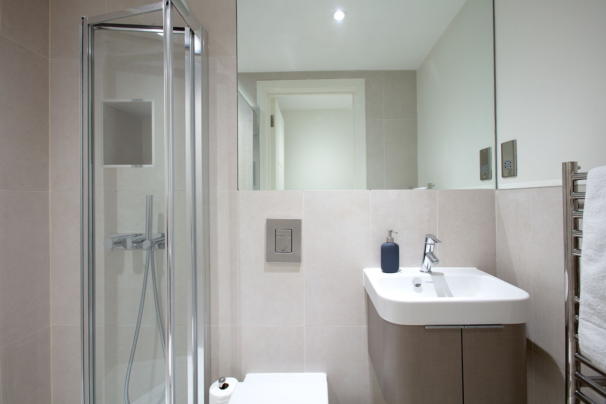 A modern bathroom with a glass shower enclosure, a white sink, and a towel rack.