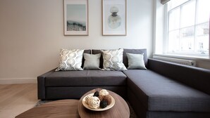 A modern living room with a grey sectional sofa, a round wooden coffee table, and two framed artworks on the wall. - Hampden Apartments - The George (Windsor)