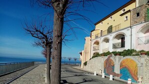 Una calle costera con acera de piedra, un árbol y un edificio con murales de colores.