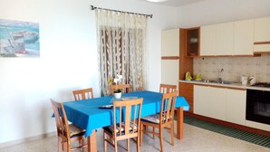 Un comedor con una mesa cubierta de azul, rodeada de sillas de madera. Hay una planta en maceta con flores sobre la mesa.