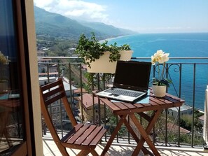 A balcony with a laptop, wooden chairs, and potted plants overlooking a coastal view. - Un Oblò sul Mare (San Lucido)