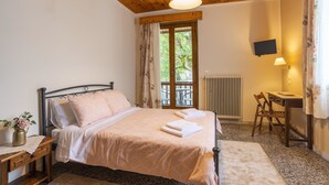 Un dormitorio con techo de madera, una cama con ropa de cama rosa, una mesita de noche con un jarrón, un escritorio con una silla y un televisor en la pared.