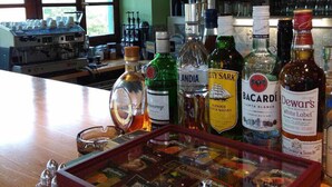 Zona de bar con varias botellas de licor, una exhibición de cajas de whisky y un ventanal con cortinas.