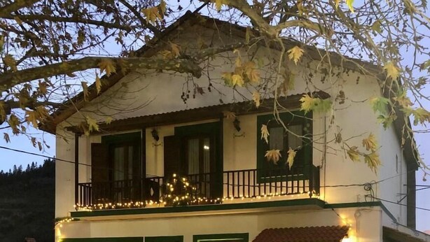 Un edificio de dos pisos con un balcón, una puerta con un cartel y un árbol de Navidad.