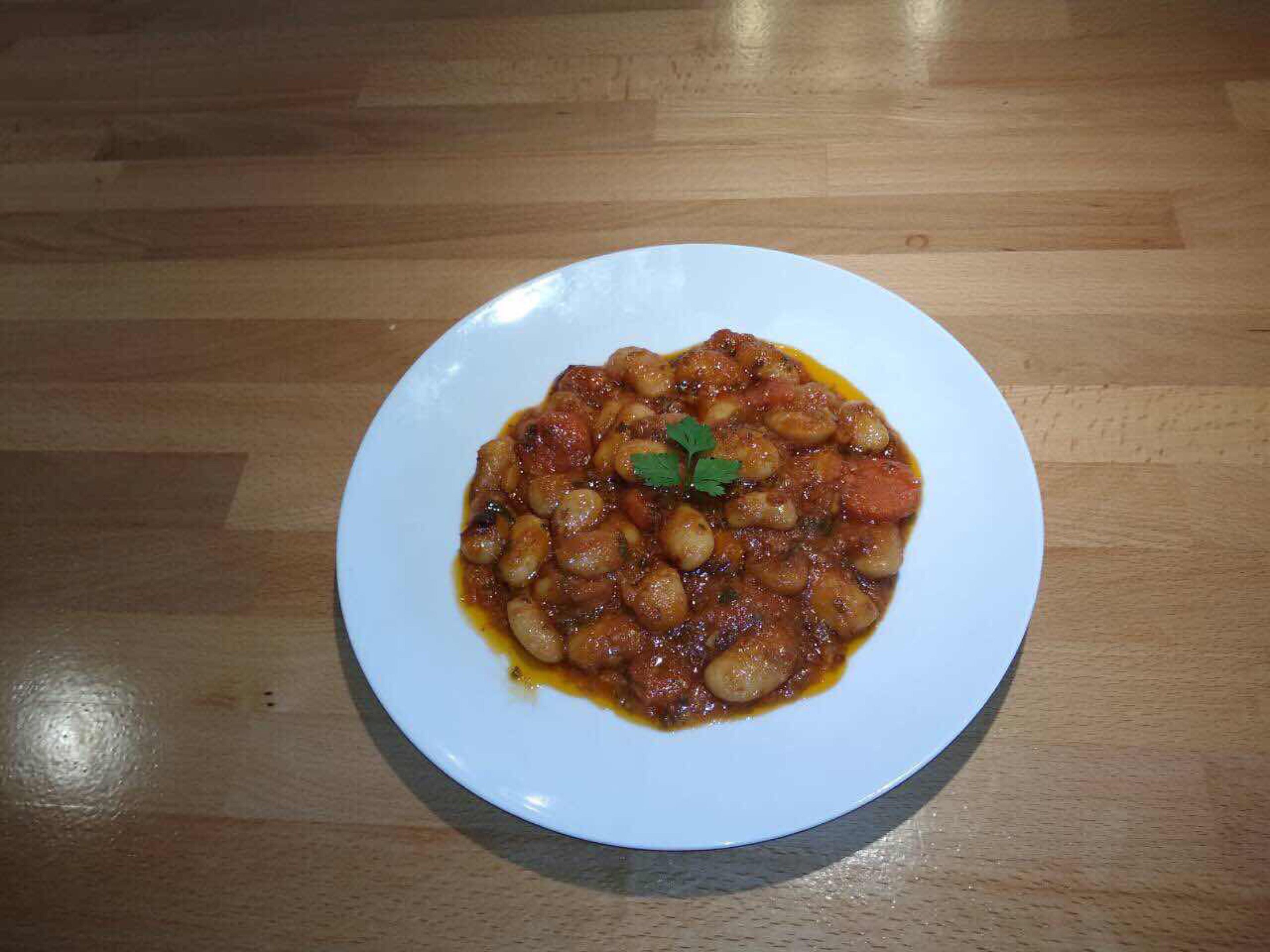 Une assiette blanche contenant un plat de haricots, posée sur une table en bois.