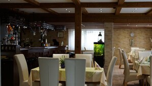 A restaurant with wooden beams, a bar area, and tables with white chairs. - Höfener Wirtshaus (Monschau)