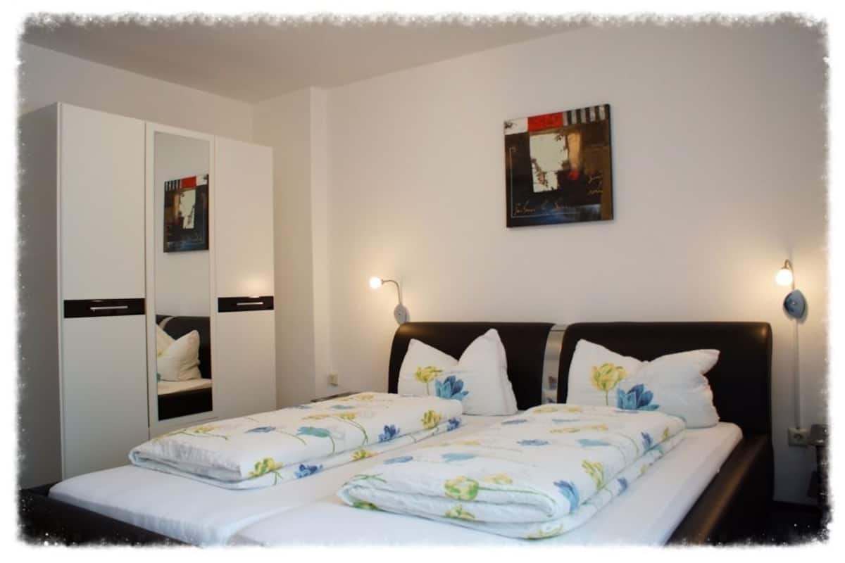 A bedroom with a bed, two bedside tables, a wardrobe, and a wall-mounted artwork.