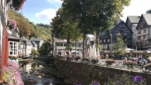 A riverside town with traditional buildings, a bridge, and outdoor seating areas. - Höfener Wirtshaus (Monschau)