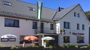 A two-story building with a sign for 'Hotel Wirslaus' and a 'Kaffee Haus' sign. There are outdoor umbrellas and a statue in front. - Höfener Wirtshaus (Monschau)