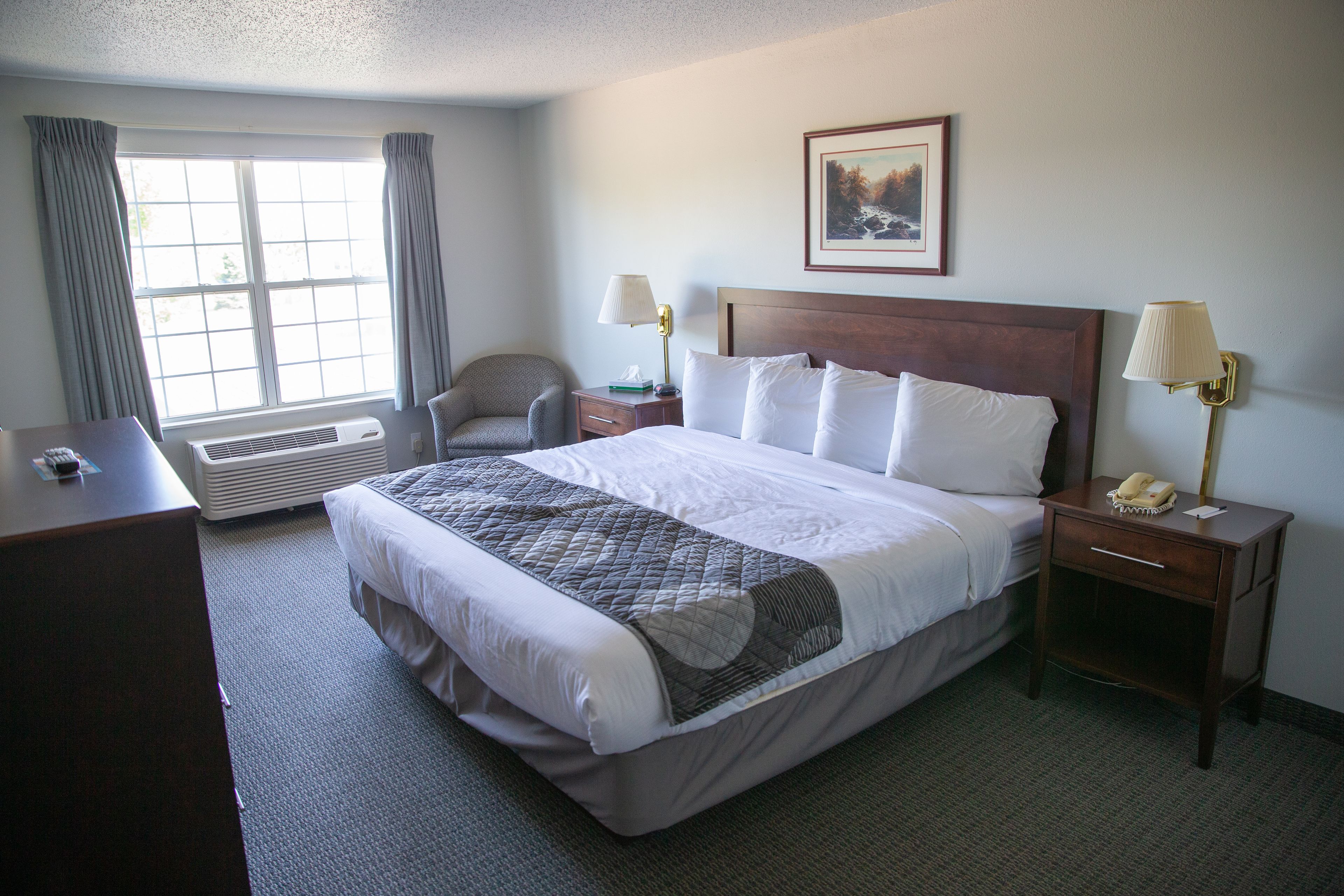 A hotel room with a large bed, two bedside tables with lamps, a chair, a desk, and a window with curtains.