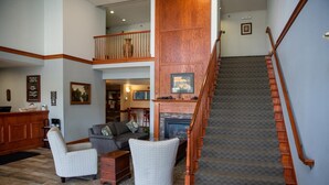A spacious living area with a fireplace, a wooden staircase, and a high ceiling. - GrandStay Hotel & Suites Hastings (Hastings)