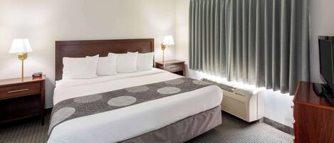 A hotel room with a large bed, two bedside tables with lamps, a TV, a heater, and a window with curtains.