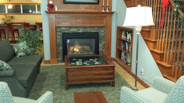 A cozy living room with a fireplace, a coffee table, and a bookshelf. - GrandStay Hotel & Suites Hastings (Hastings)