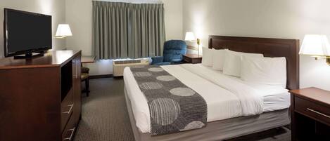 A hotel room with a bed, a desk with a television, a chair, a lamp, and a window with curtains.