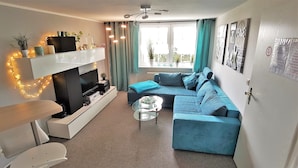 A modern living room with a sofa, a coffee table, a TV on a stand, and a fireplace. - Parklife Apartments (Winterberg)