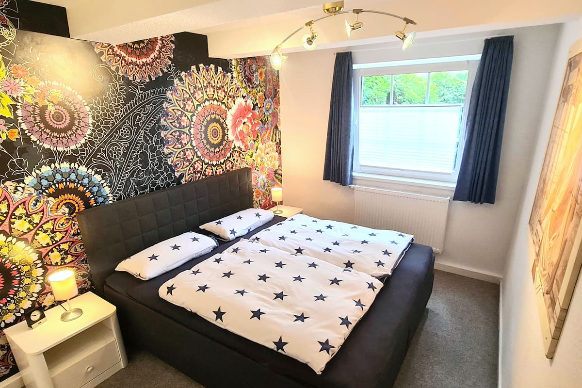 A bedroom with a bed, nightstand, and a wall tapestry.